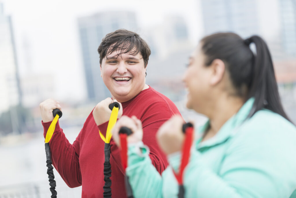 Young adult man with friend outside exercising using exercise bands.